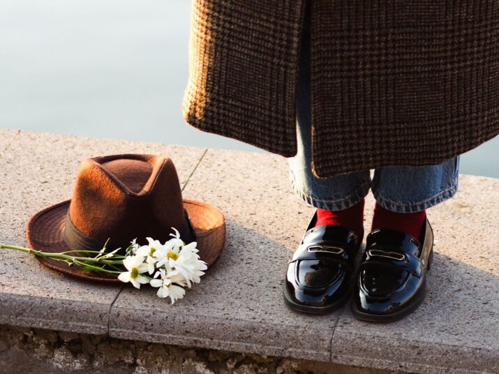 Close-up of a stylish outfit with shoes, hat, and daisies by a riverside.
