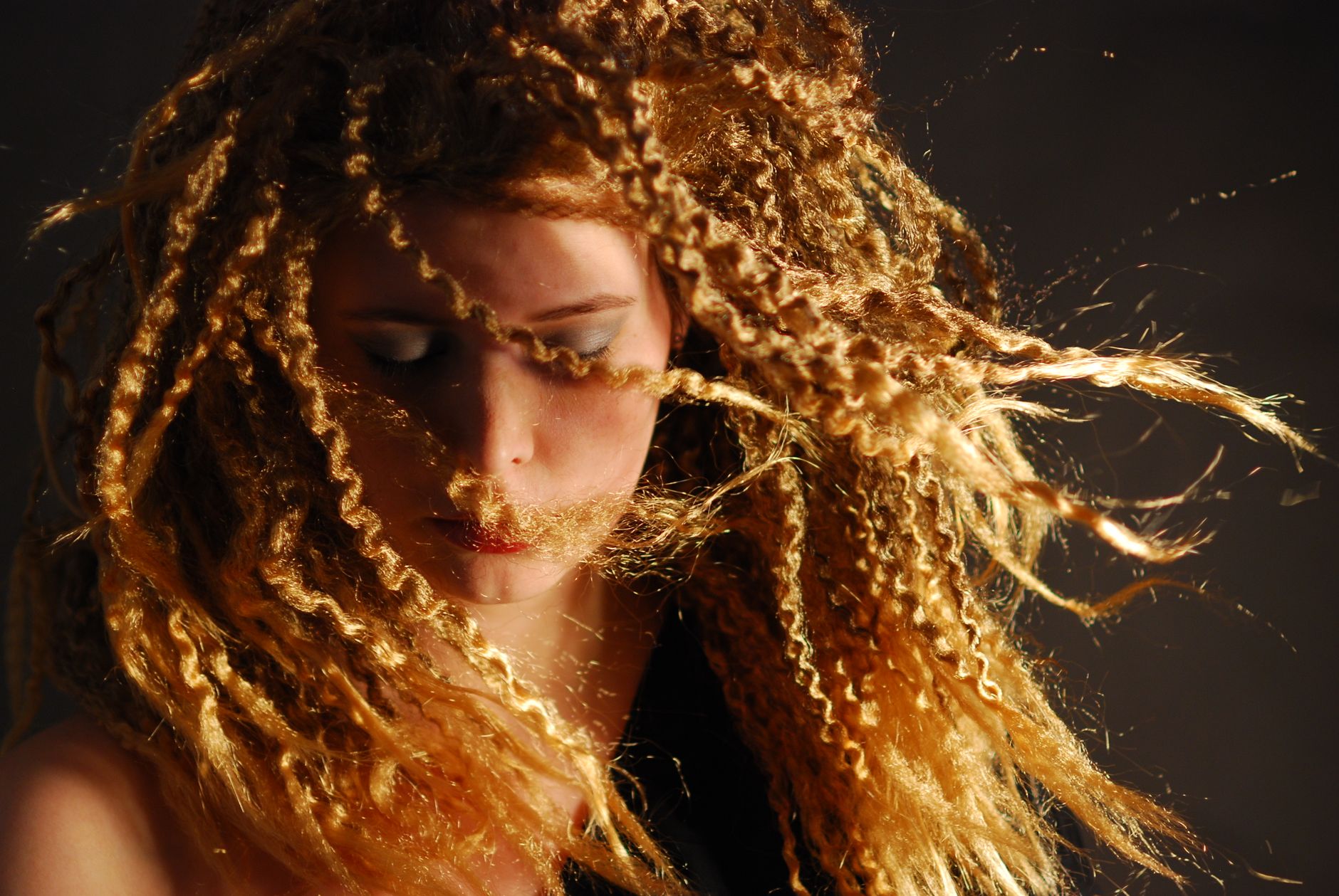 Artistic portrait of a woman with dynamic curly hair against a gray background.