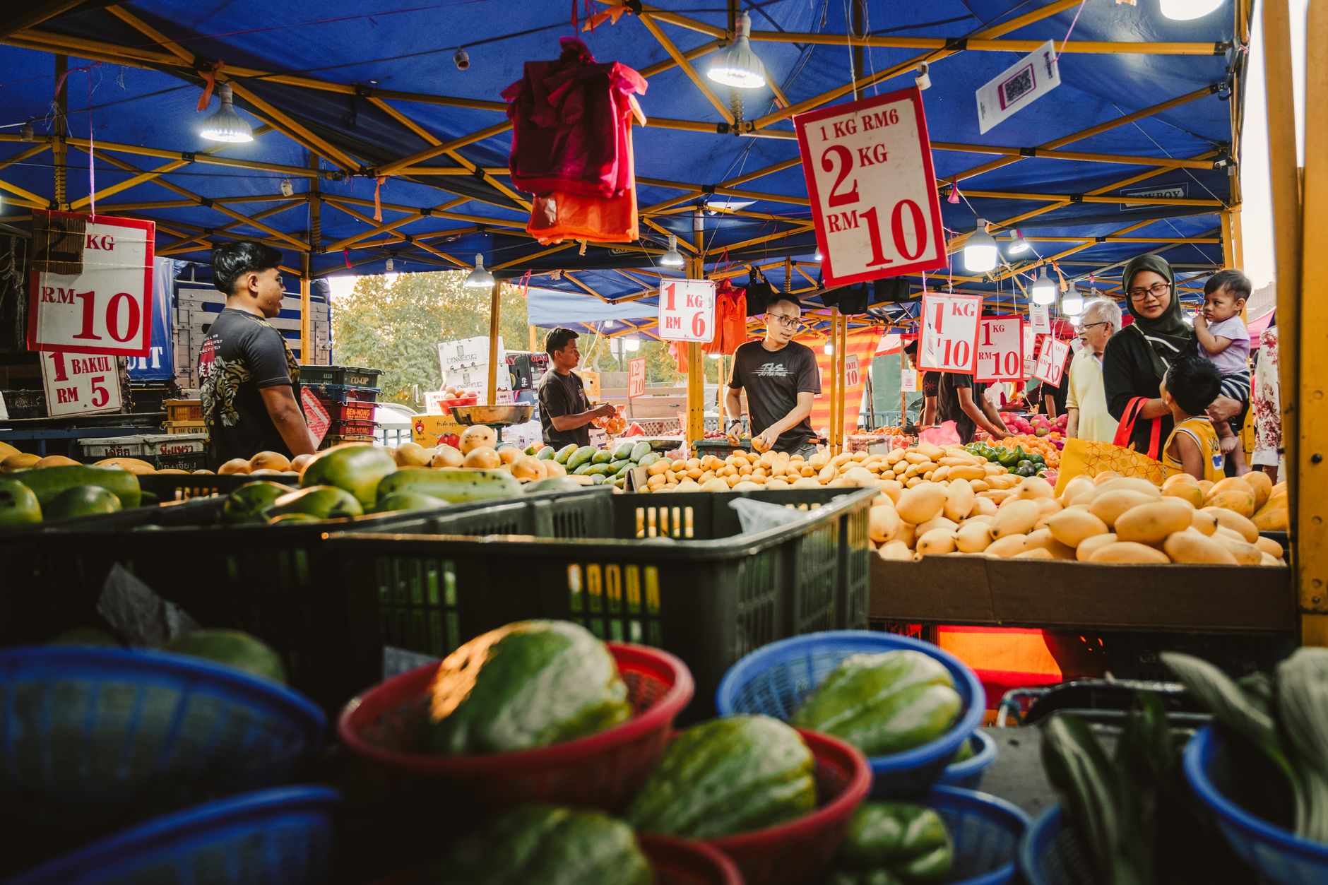 A bustling night market in Sepang, Malaysia, showcasing a variety of fresh produce under colorful canopy lights.