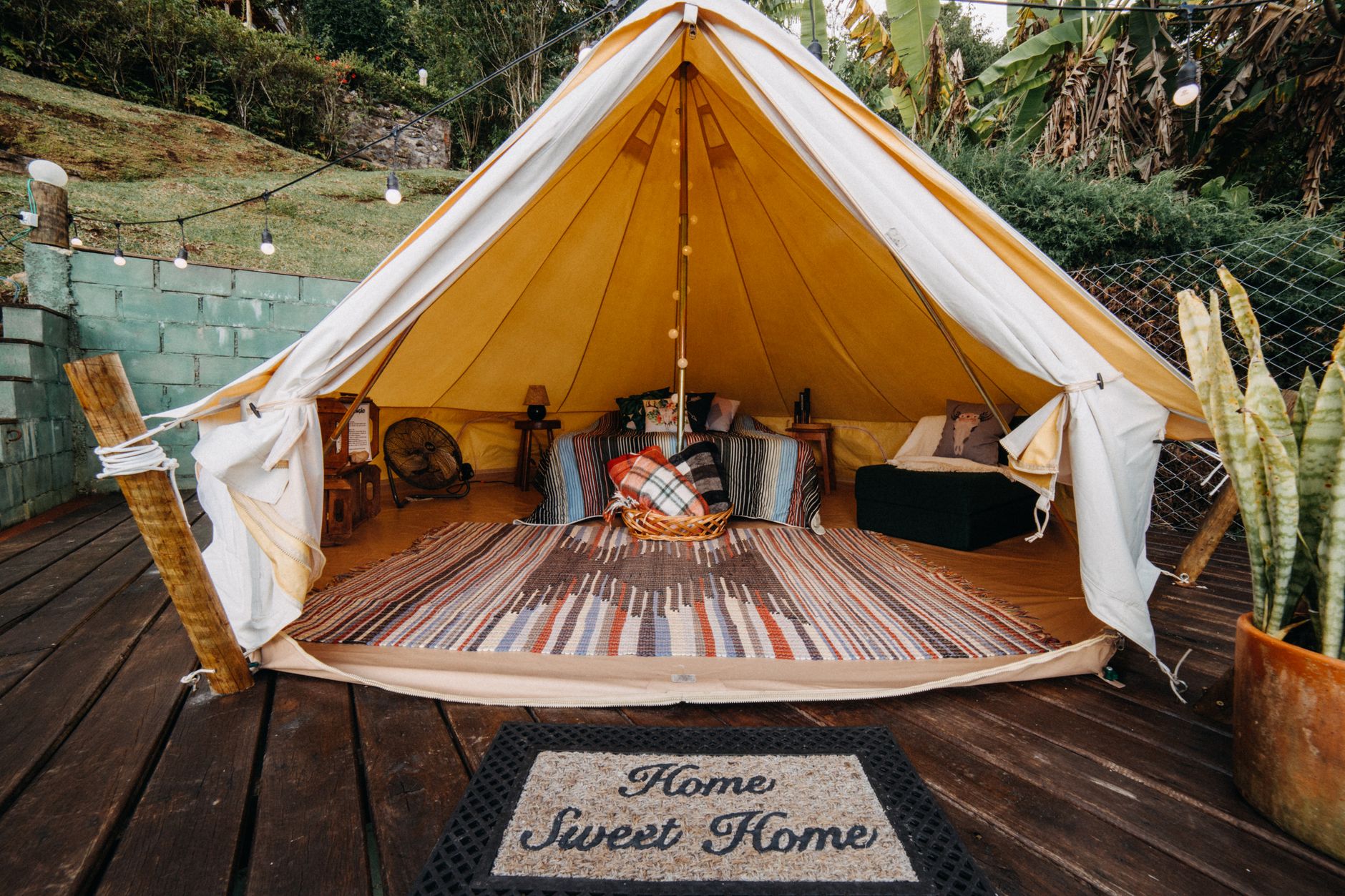 Tent with colorful carpet and comfortable seats located on wooden veranda with rug in rural area with lush green trees