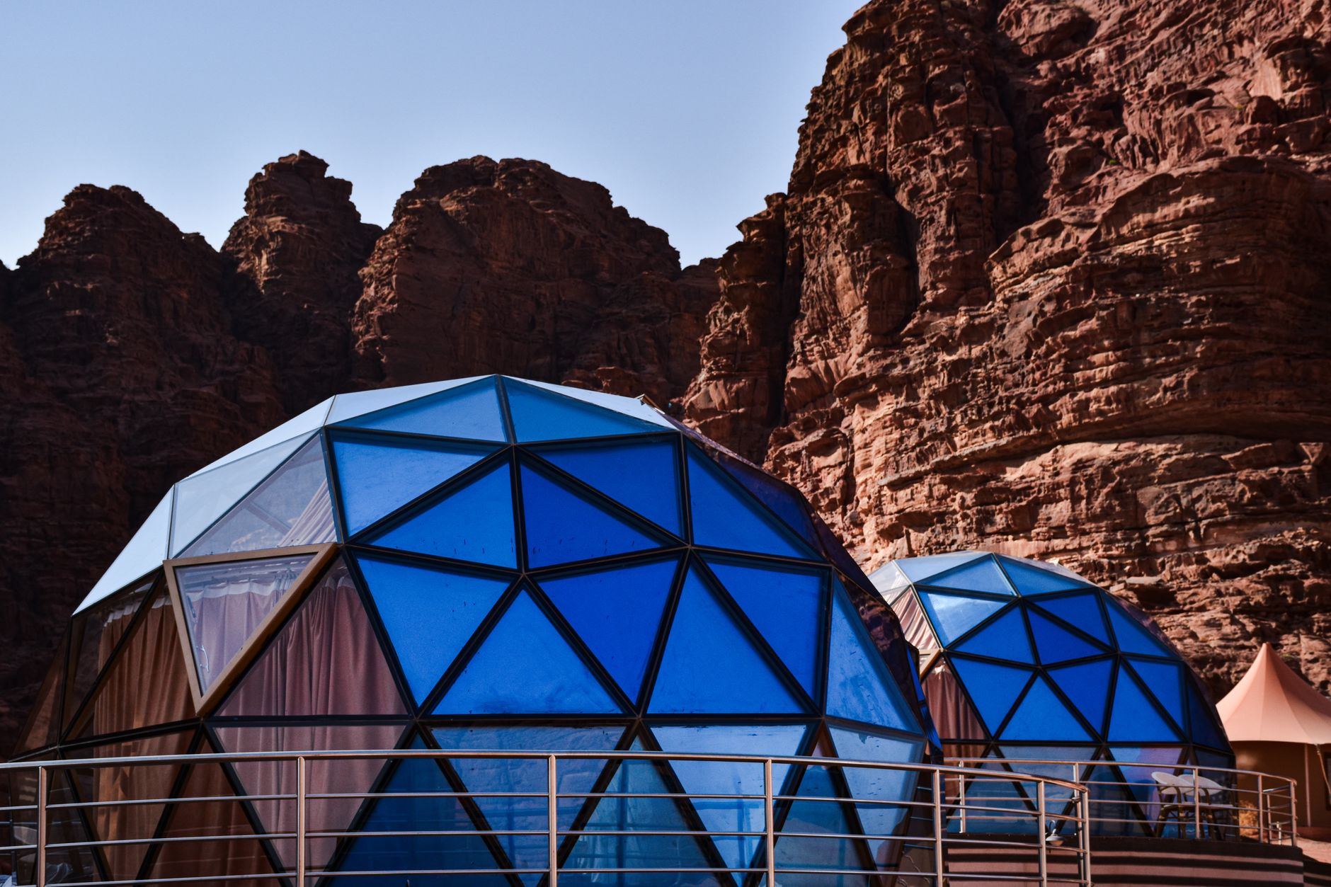 Geodesic dome structures with blue glass set against a dramatic red rock canyon landscape.