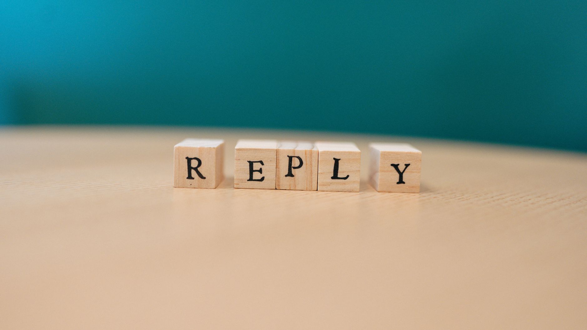 Close-up of wooden blocks spelling 'REPLY' over a wooden surface.