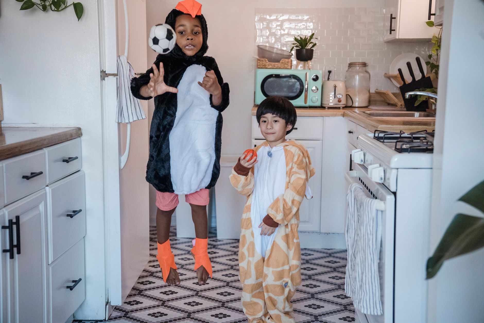 Kids in penguin and giraffe costumes having fun indoors with a ball.
