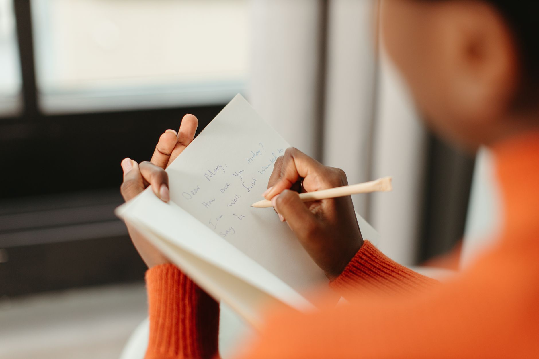 A woman writing a close-up letter in a notebook with a pencil and a blurred background.