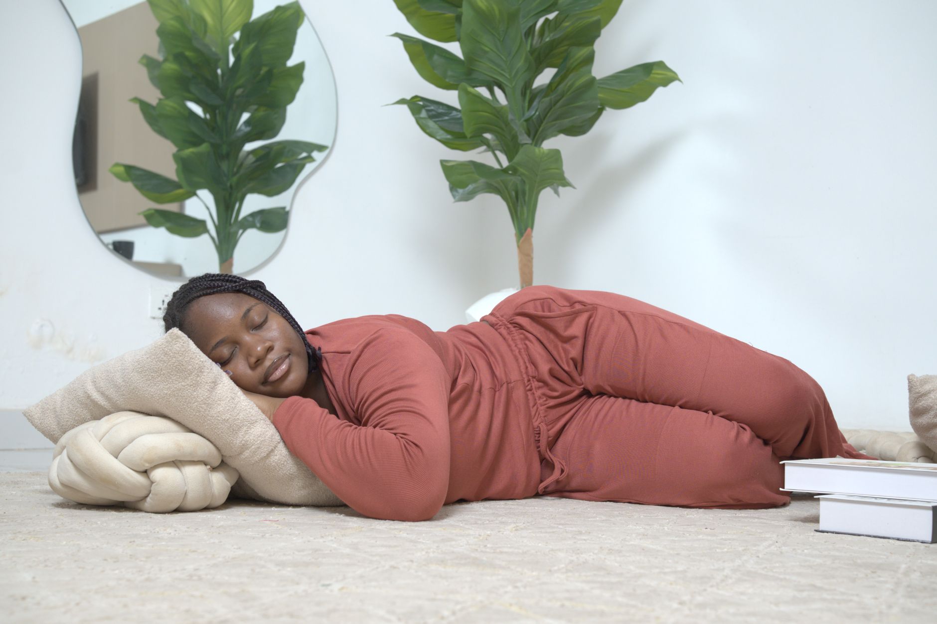 A woman peacefully lying indoors surrounded by plants and cushions, exuding relaxation.