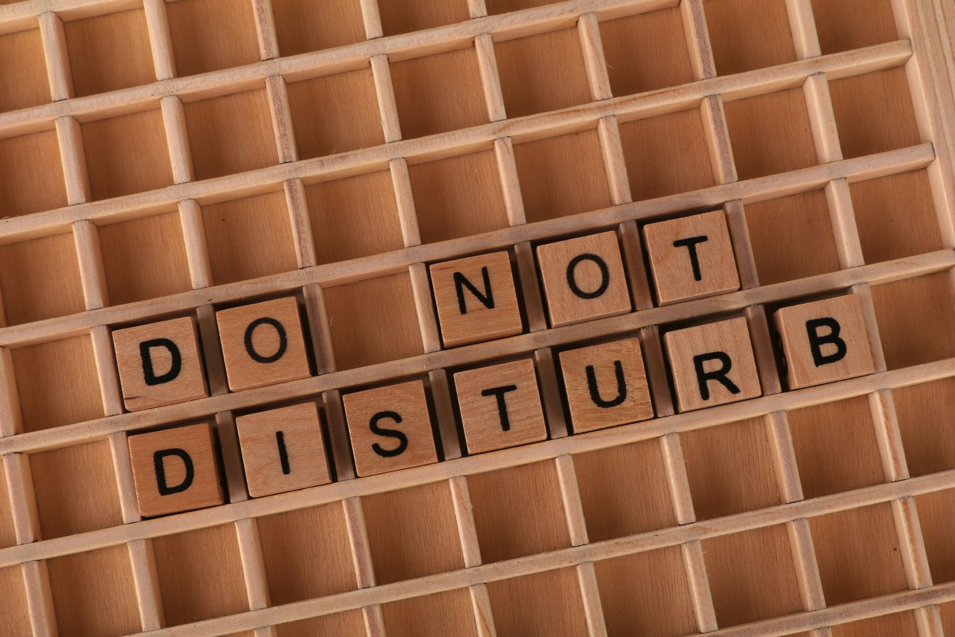Wooden Scrabble tiles arranged on a grid spelling out 'Do Not Disturb' for privacy concept.