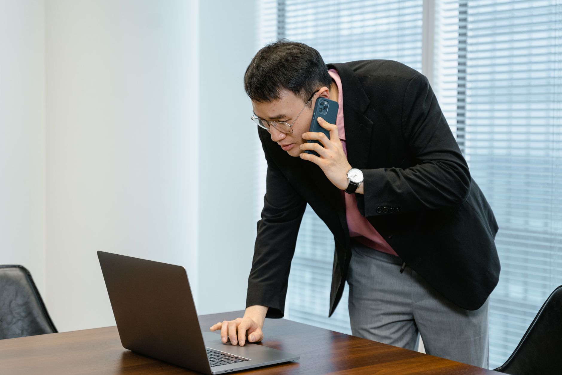 Asian businessman in the office multitasking with a laptop and smartphone call.