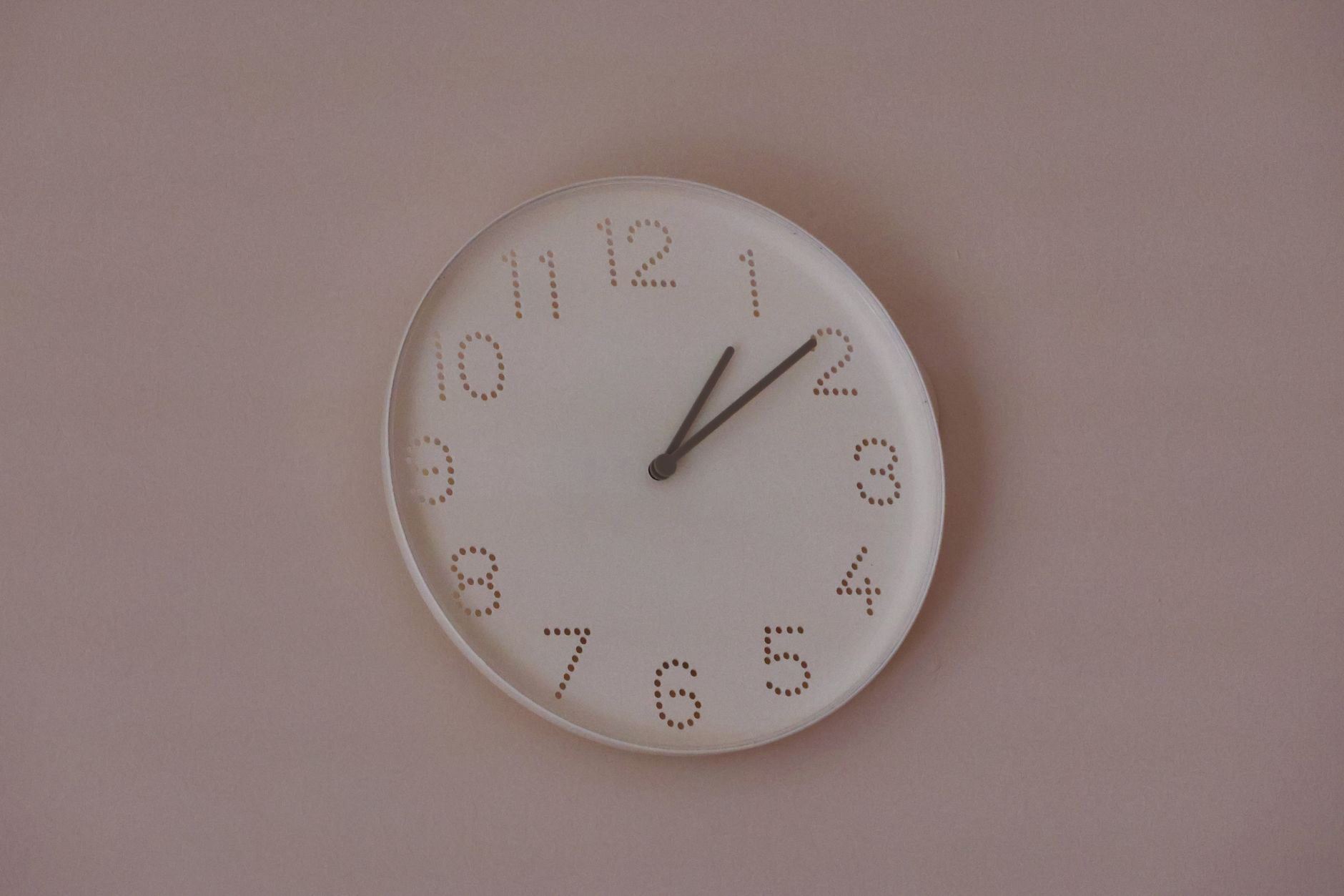 A minimalist wall clock with dot numbers on a pastel wall, shot indoors.
