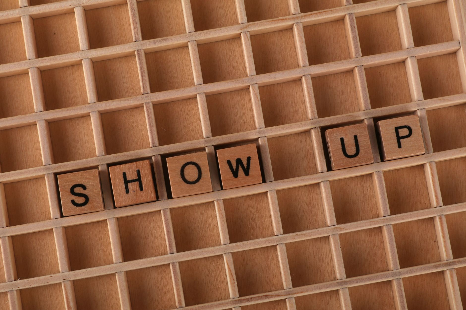 Flat lay of wooden letter blocks spelling 'Show Up' on wooden grid for motivation.