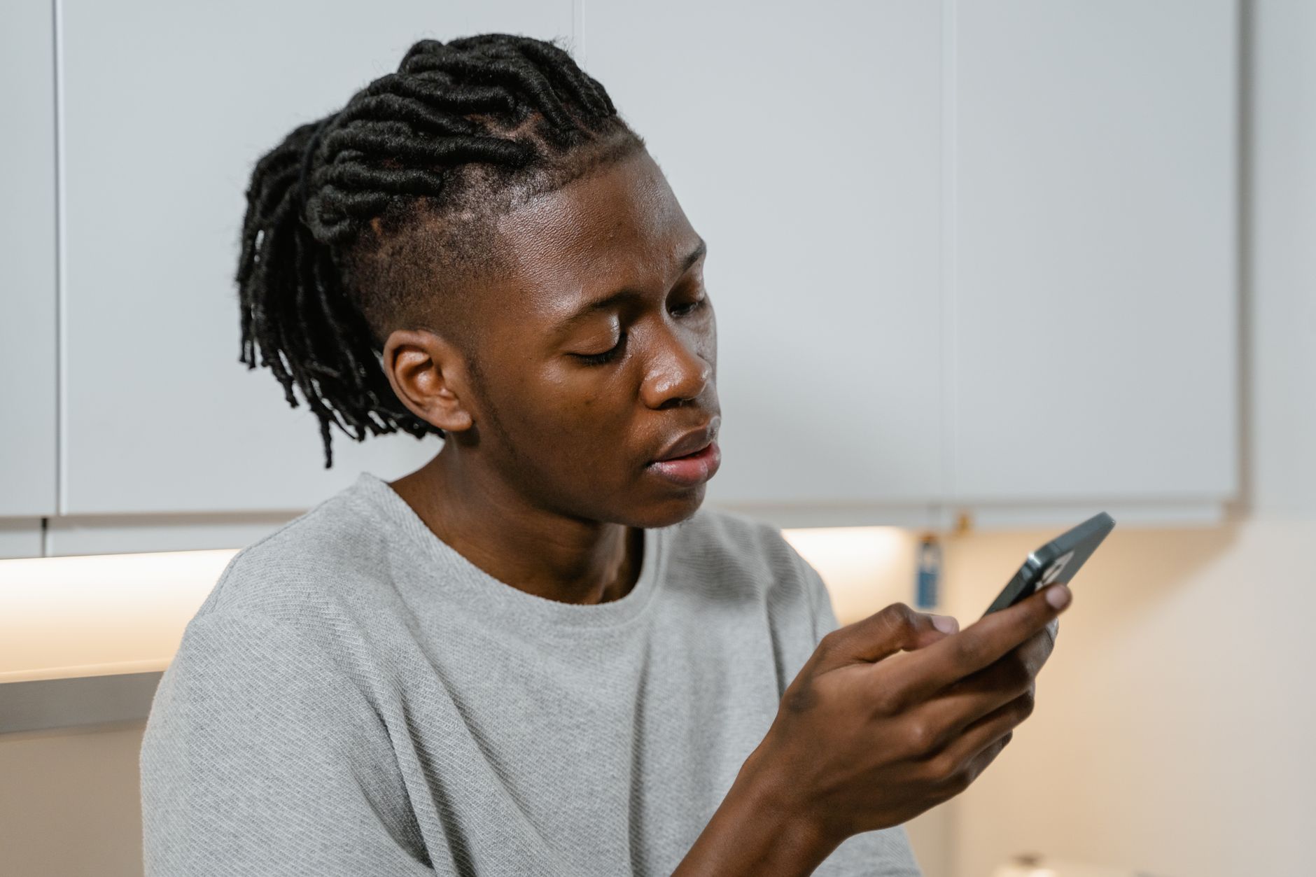 Young man with braided hair checking his smartphone while at home, embodying modern lifestyle.