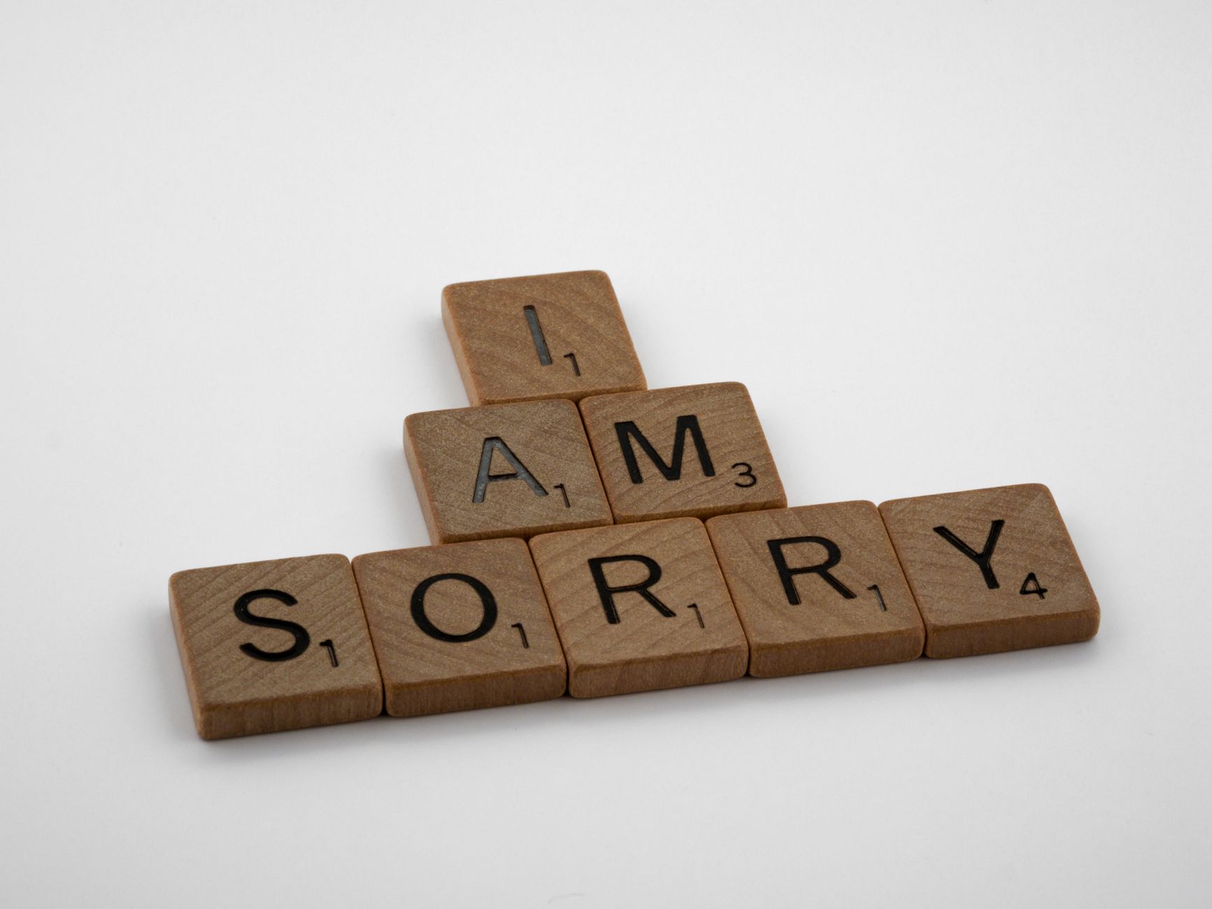Wooden Scrabble tiles arranged to say 'I Am Sorry' on a clean white background, conveying a message of apology.