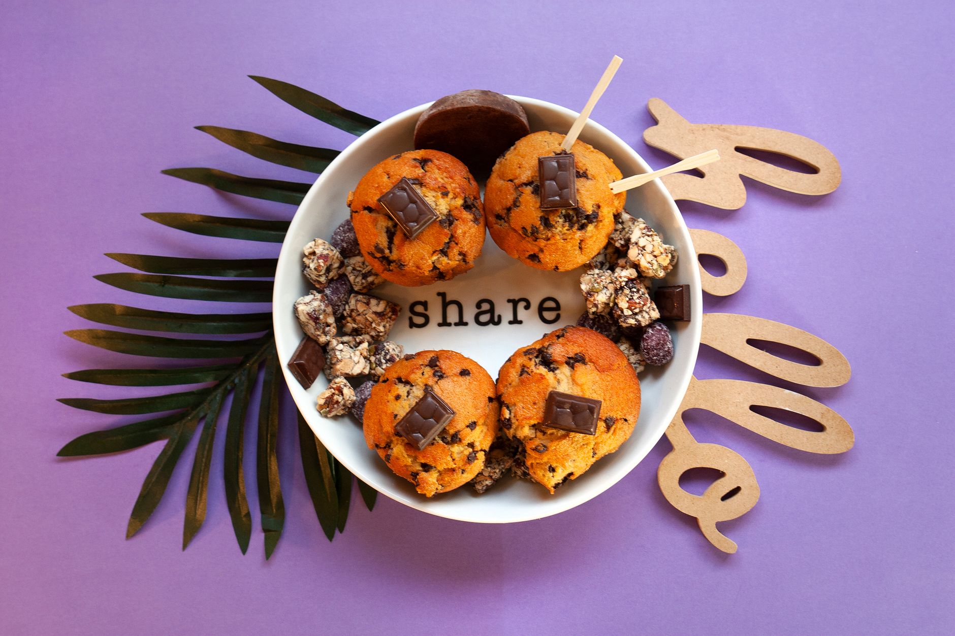 Top view of homemade chocolate chip muffins with chocolate pieces on a purple backdrop, perfect for sharing.