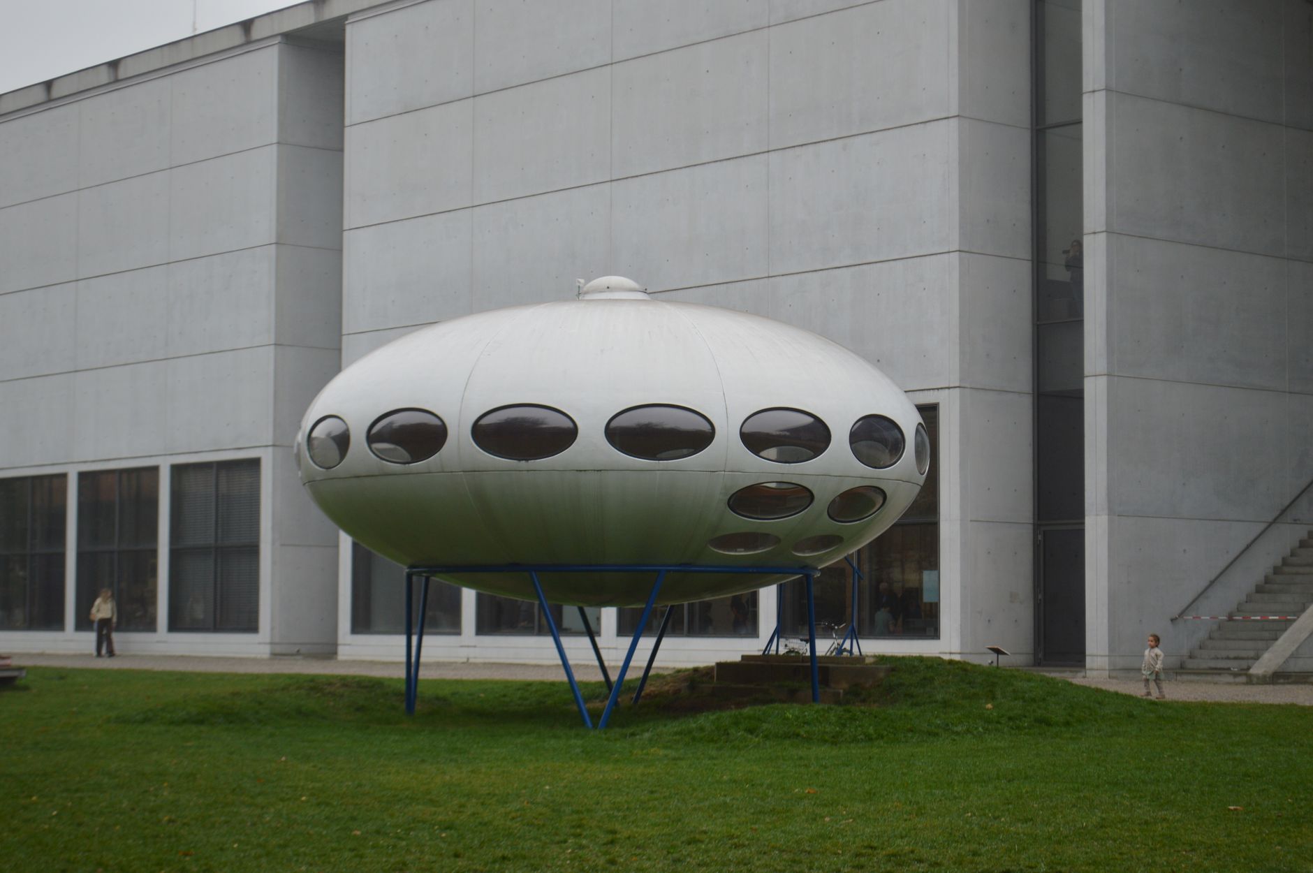 Modern UFO-like structure outside a contemporary building on a foggy day.