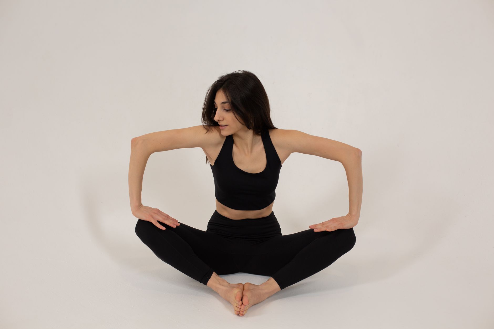 Full body of slim female athlete in sportswear sitting in butterfly pose and pressing on knees for stretching legs