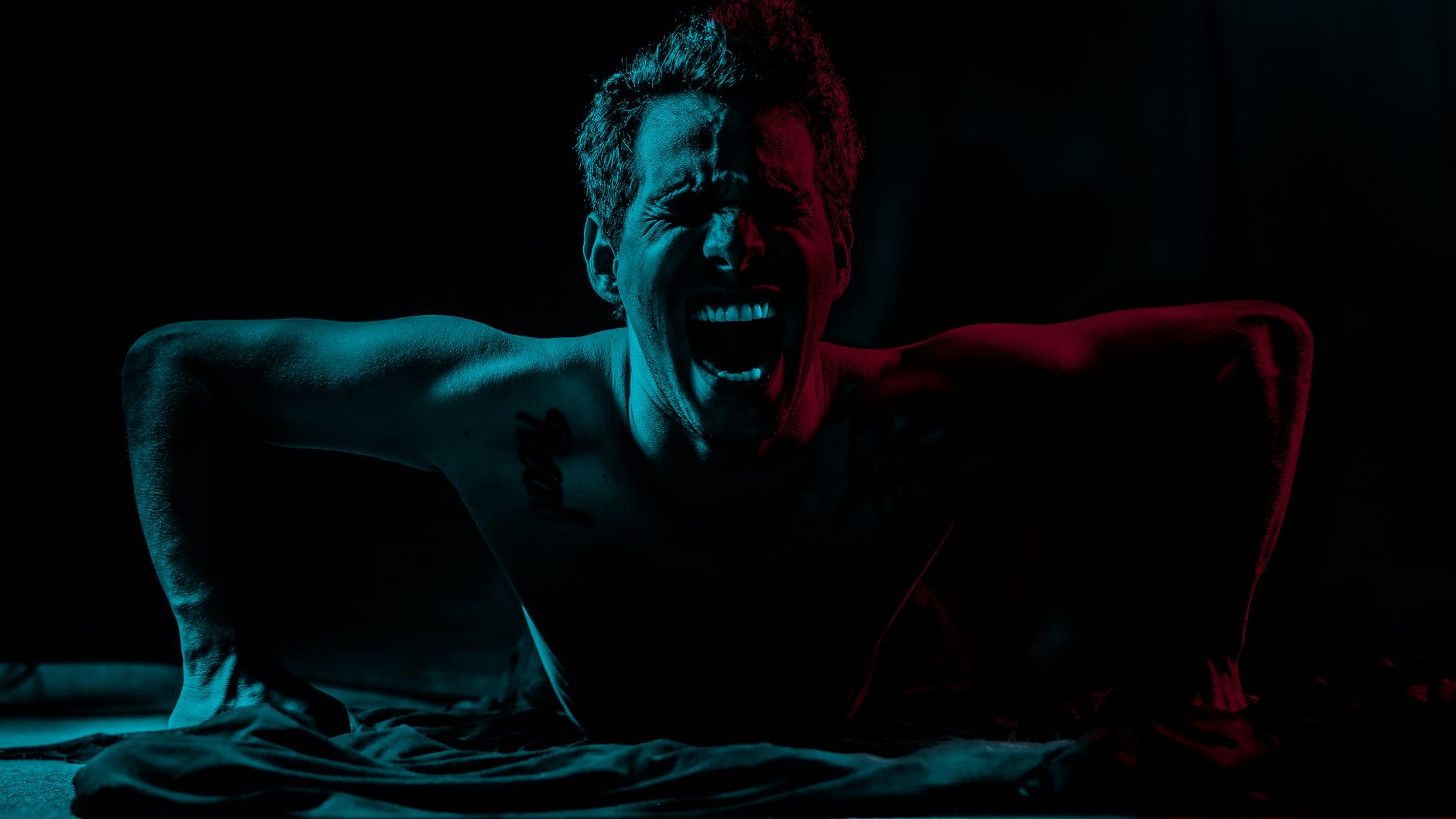 Artistic portrait of a man screaming under dramatic colored lighting, conveying intense emotion.