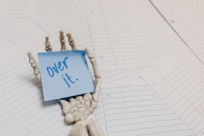 A conceptual image of a skeleton hand holding a sticky note reading 'over it' on lined paper.
