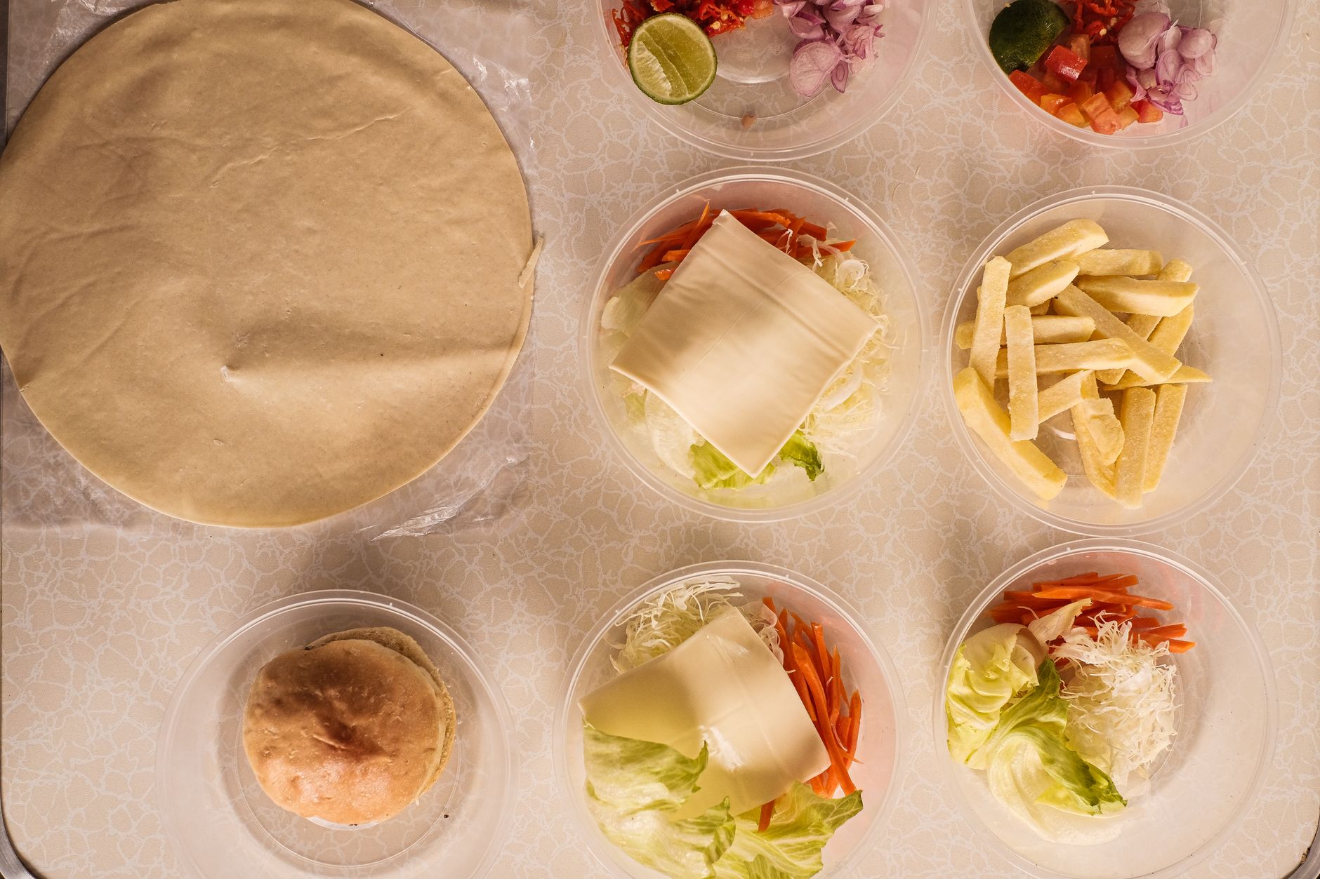 Top-down view of burger ingredients and dough on a table, ready for assembly.