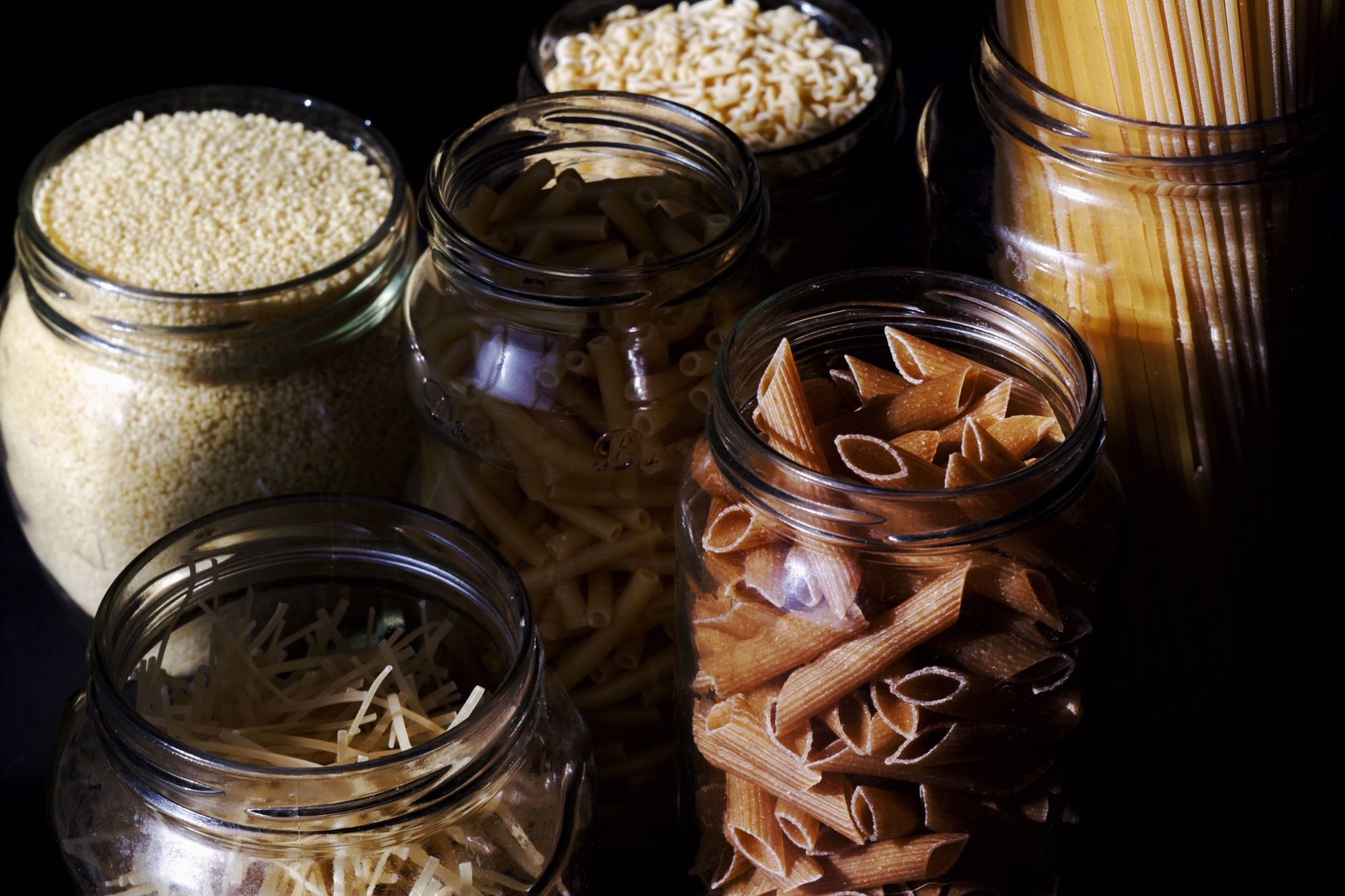 Different types of pastas and cereals in glass jars on kitchen in sunlight