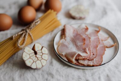Raw pasta, garlic, and bacon on a table, ready for a delicious meal.