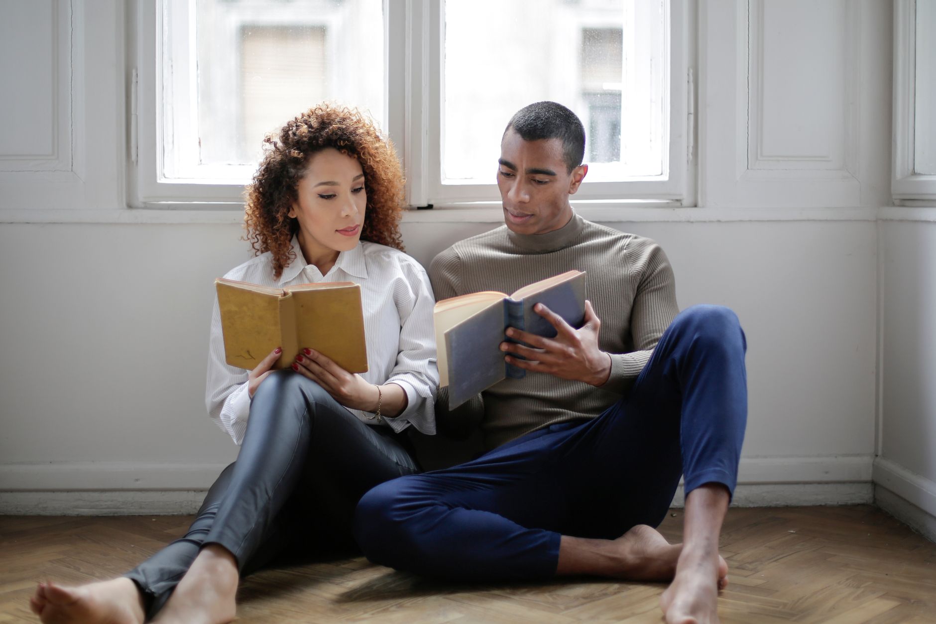 Young couple enjoying a quiet reading session at home, seated by the window.